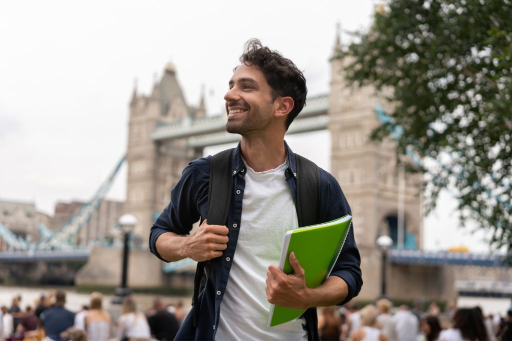 A student in London with Tower Bridge behind him. International students in the UK often experience expat homesickness.