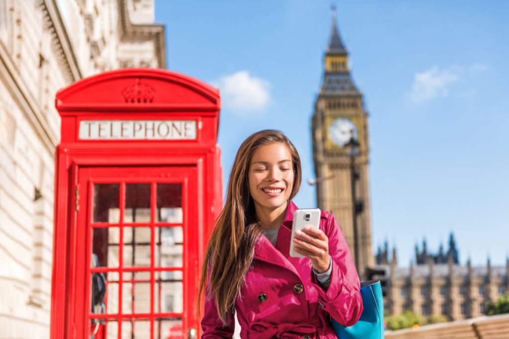 Woman stands in front of a red telephone box in London with Big Ben in the background.