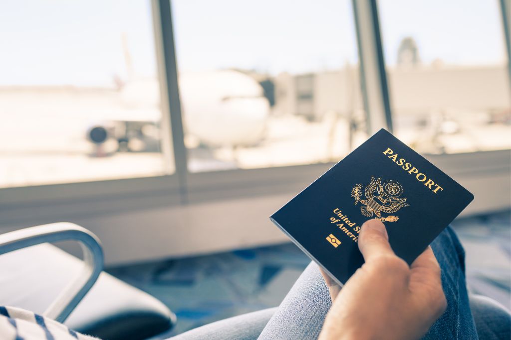 Person sitting in an airport holding a US passport. Visiting home can sometimes help with expat homesickness.