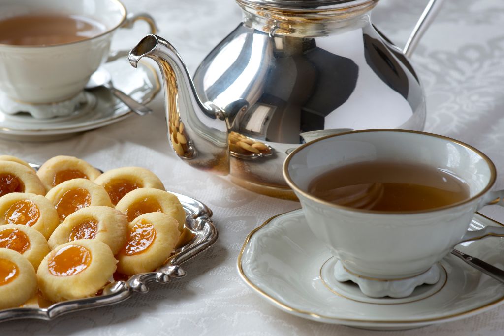 Tea service featuring a steel pot next to a plate of jam biscuits. Tea leaves are an iconic souvenir from England.