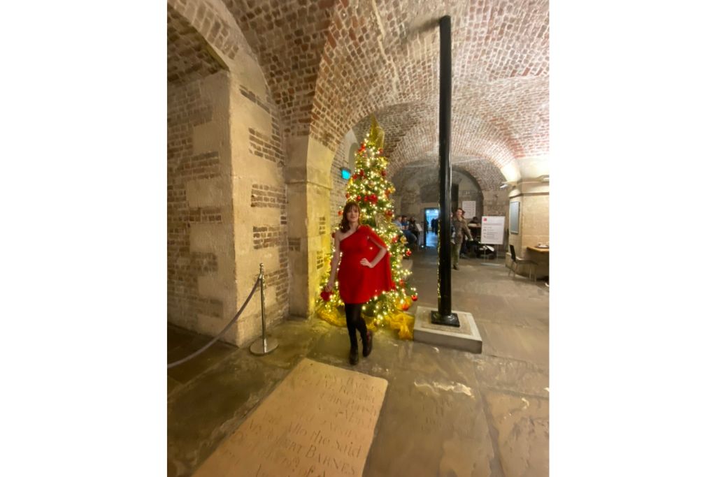 Cafe in the Crypt at St-Martins-In-The-Fields London. Girl in a red dress stands just behind a crypt memorial marker and in front of a decorated Christmas tree.