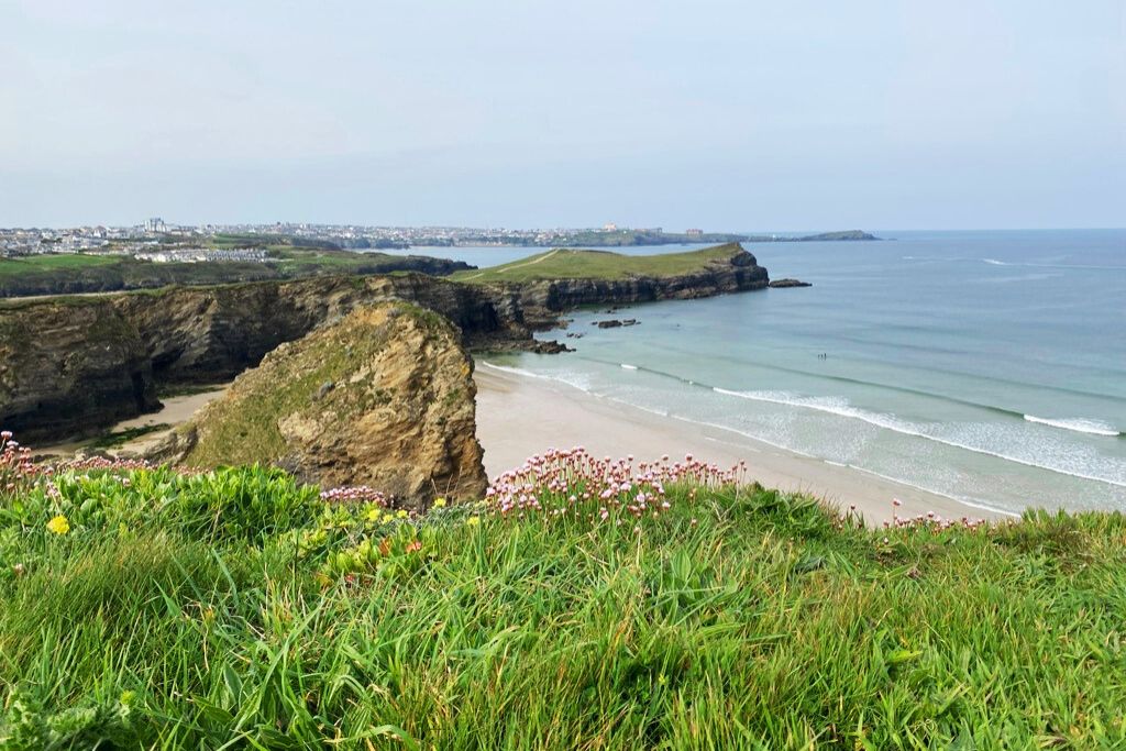 View toward Newquay Cornwall from the Southwest Coastal Path. Green grass on the hillside looking down toward a sandy cove beach.