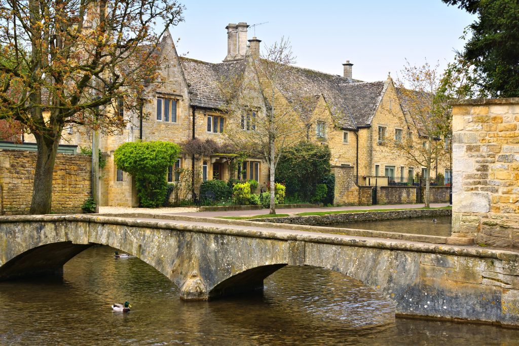Bourton-on-the-Water arched stone bridge over the River Windrush with stone houses in the background. This 3 day Cotswold itinerary is based in Bourton-on-the-Water.
