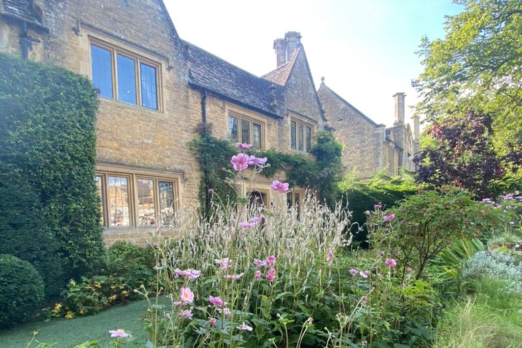 Honey stone cottage in the Cotswolds with pink flowers in the garden.