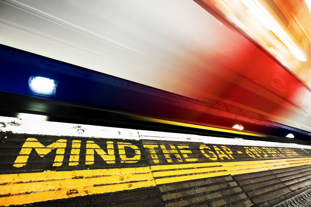 Ground markings that read "Mind the Gap" as a train passes the London Underground platform.