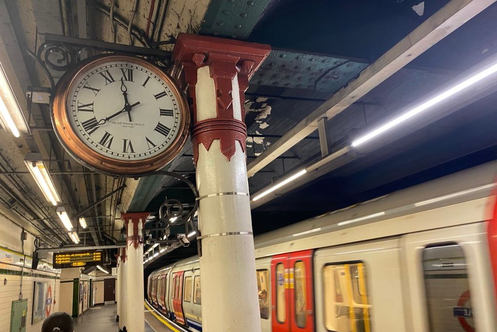 Clock above London Underground station platform as train passes by.